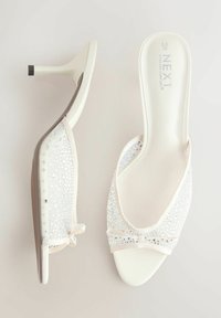 Mules blanches pour femmes à talons hauts avec tige en mesh, décorées de petits strass et d'un détail nœud sur la bride avant.