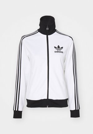 Hvit zip-up jakke med høy krage, sorte detaljer og tre svarte striper på ermene. Inkluderer et Adidas-logo på venstre bryst.