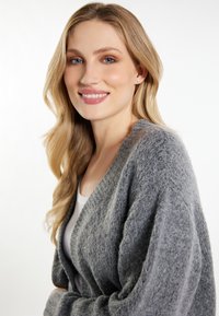 Cardigan gri, texturat, cu un croi lejer și mânici largi. Purtați peste un top alb, având un aspect moale și pufoș.