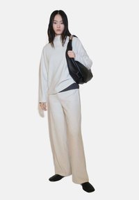 Pulover oversized de culoare crem și pantaloni evazați dintr-un material moale, asortați cu o geantă din piele neagră și pantofi slip-on negri.