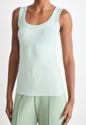 Bezrękawnik w jasnym zielonym kolorze z prążkowanego materiału, noszony z pasującymi, luźnymi spodniami na osobie stojącej na jednolitym tle.