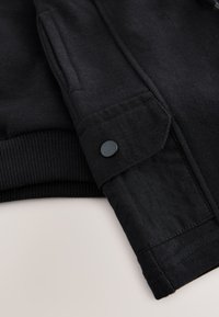 Black hoodie featuring a smooth texture with a ribbed hem and sleeve cuffs, button detail on the sleeve, and a slightly loose fit.
