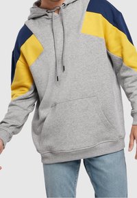 Sweat à capuche gris avec accents bleu marine et jaune, capuche à cordon, poche kangourou et poignets côtelés. Fabriqué en tissu de sweat-shirt doux.