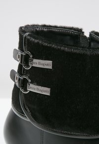 Botas negras con un upper de pelo suave y dos detalles de hebilla plateada, y un inferior de cuero liso. Etiquetas metálicas de marca visibles en las hebillas.