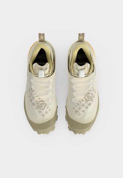 Ζευγάρι μπεζ παπούτσια χωρίς κορδόνια με ανθεκτικές σόλες, αριθμητικό σχέδιο στο πάνω μέρος και θηλιές στα τακούνια, σε λευκό φόντο.