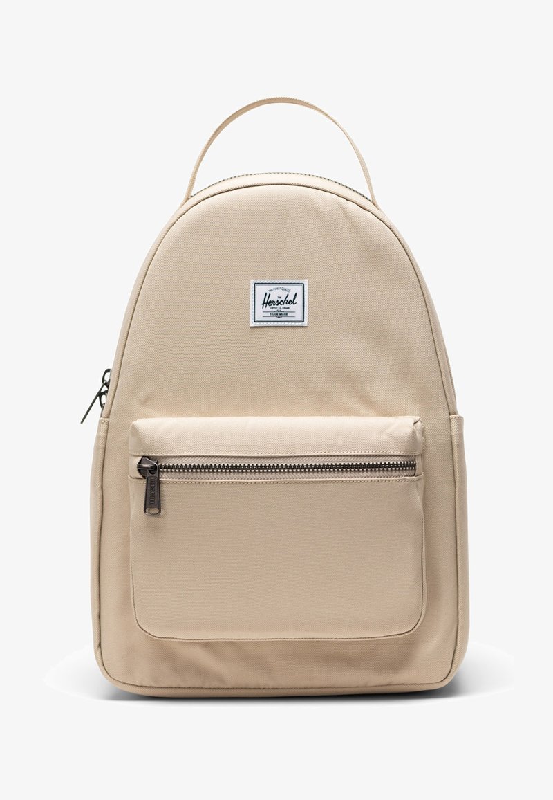 Sac à dos beige Herschel avec poignée supérieure, poche avant zippée et écusson de marque rectangulaire centré au-dessus de la poche.