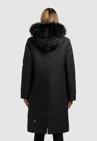 Sort lang puffjakke med hætte, der har en pelskant. Glat tekstur og slankt design, med knapper i bunden og branding på siden.