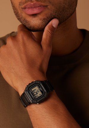 Digitaluhr von Casio mit schwarzem Gummiband, quadratischem Ziffernblatt, digitaler Anzeige für Uhrzeit und Datum, akzentuiert mit roten Details.