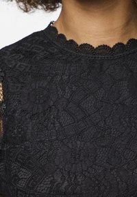 Tessuto in pizzo nero con motivi floreali, scollo a scallop e elementi di design intricati, creando un aspetto tessurizzato e stratificato.