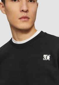 Zwart sweatshirt met een ronde hals, voorzien van een witte logo-accent op de borst. Gladde katoenen stof met een relaxed fit.