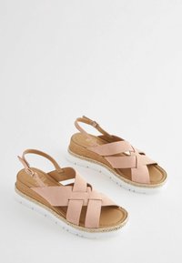 Sandale cu toc wedge din suede roz deschis, cu curele încrucișate, cataramă la gleznă, talpă albă și finisaj din jute în jurul platformei.