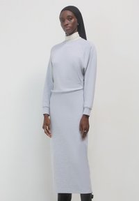 Helles graues, langärmliges Kleid aus einem weichen Stoff mit lockerer Passform, das einen hohen Ausschnitt und gerippte Akzente aufweist. Durchgehend glatte Textur.