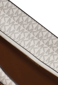 Pochette in pelle beige con motivo a logo "MK" perforato ripetuto e zip dorata su fodera interna marrone.