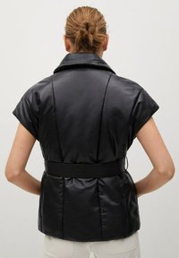 Czarna kurtka z faux skóry z krótkimi rękawami, szwami na ramionach, szerokim kołnierzem i dopasowaną talią podkreśloną paskiem. Gładka tekstura, minimalistyczny design.