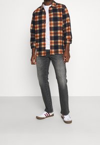 Camisa de franela a rayas en naranja, azul marino y gris; camiseta blanca debajo; jeans grises; zapatillas blancas con rayas rojas.
