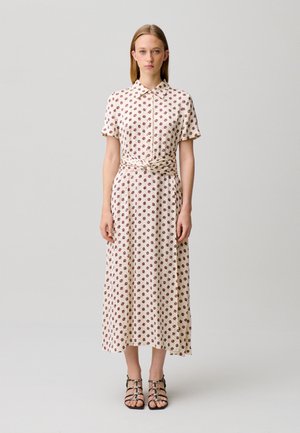 Donna con capelli castani lisci indossa un vestito midi color crema con piccolo motivo floreale rosso, maniche corte, un colletto e sandali neri con lacci.