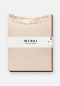 Beige og marineblå t-shirt sæt, foldet med en orange accent. Vist med en hvid label, der har brandnavnet og teksten: "To er bedre end én."