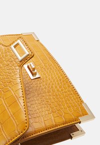 Gros plan sur un sac à main en cuir jaune texturé avec des ferrures dorées, comprenant un fermoir rectangulaire et des protège-coins.