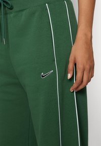 Gröna träningsbyxor med vita sidostråk och en svart Nike-logotyp. Tillverkade av mjukt material, designen inkluderar en elastisk midja och dragsko.