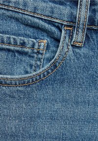 Gros plan sur un tissu en denim bleu avec une poche avant et un passant de ceinture ornés de détails en couture orange.