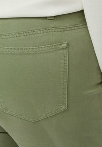 Pantalon vert olive avec une poche arrière présentant une couture droite, une texture lisse et une coupe ajustée.