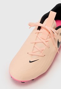 Nike foci cipő világos rózsaszínű, texturált felső résszel, fekete fűzőkkel és fekete logóval. Élénk rózsaszín talppal rendelkezik a tapadás érdekében.