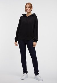 Sudadera negra con cordón, corte relajado y mangas largas. Combinada con jeans azul oscuro y zapatillas blancas. Textura suave.