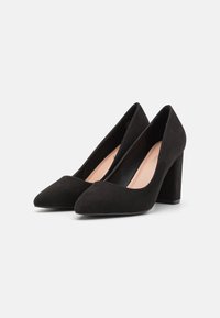 Escarpins en suède noir avec un bout pointu et un talon épais. Texture lisse avec un design minimaliste. L'intérieur est doté d'un revêtement nude.