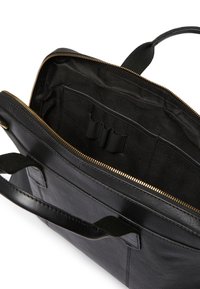 Svart läder tote-väska med dragkedjestängning, som har en texturerad insida med fickor och öglor för organisation. Detaljer i guldfärgad metall.