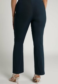 Marinblå utsvängda byxor i stretchigt material, med en jämn yta, midjehögt liv och en ren klippkant, parat med ljusa sandaler.