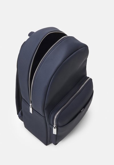 Sac à dos en polyester bleu marine avec deux compartiments zippés, surface texturée et métal argenté. Comprend un dos rembourré et des bretelles réglables.