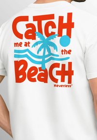 White T-shirt featuring bold red and blue graphic text: "Catch me at the Beach" with a palm tree and wave design. Brand name: Neverless.