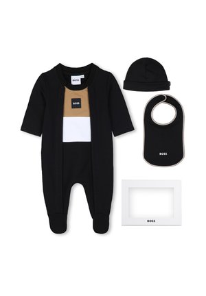 Combinaison noire pour bébé avec panneaux de poitrine marron clair et blancs, bonnet noir assorti, bavoir noir avec bordure blanche et cadre blanc marqué.