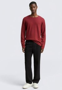 Bordeauxrode geribbelde trui met lange mouwen, gecombineerd met zwarte broek met wijde pijpen en witte sneakers. Eenvoudig ontwerp met een ronde hals en een losse pasvorm.