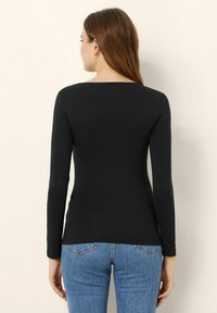 Schwarzes Langarmoberteil mit quadratischem Ausschnitt, glatter Textur und taillierter Passform, kombiniert mit hellblauen Jeans.