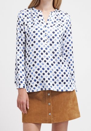 Blusa de manga larga en satén blanco con lunares azules y navy, con escote en V y botonera, combinada con una falda de ante marrón.