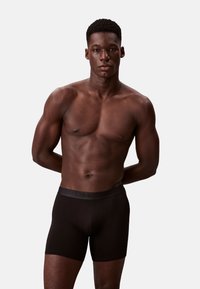 Czarne bawełniane bokserki z gładkim pasem w talii, na którym widnieje logo "Calvin Klein", prezentowane na modelu o umięśnionej budowie ciała.