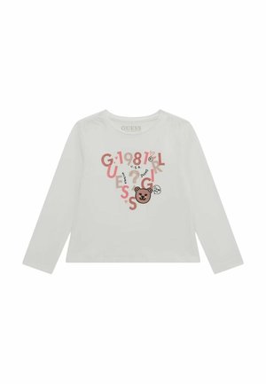 Chemise blanche à manches longues avec des lettres et chiffres rouges et beiges mélangés, un visage d'ours, et «GUESS 1981» imprimé sur le devant.