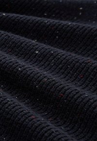 Dunkelblaues gestricktes Gewebe mit gerippter Textur und kleinen roten, weißen und blauen Farbtupfern, die verstreut sind.