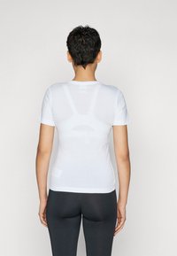 Hvit tettsittende t-skjorte med korte ermer, glatt tekstur, rund halslinning og minimale sømmer, sammen med svarte tights.