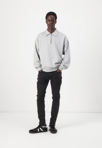Sweatshirt cinza com fecho, colarinho dobrável, com um ajuste largo, combinado com jeans skinny pretos e ténis pretos com detalhes brancos.