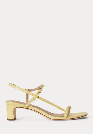 Gelbe Sandale mit niedrigem Absatz, dünnen Riemen, Knöchelschnalle und offenem Zehenbereich auf weißem Hintergrund.