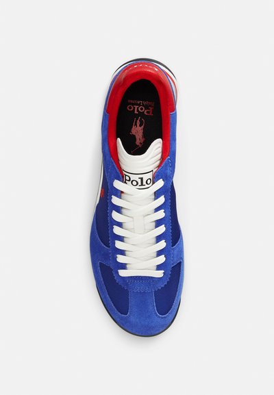 Niebieski zamszowo-materiałowy sneaker z białymi sznurowadłami, czerwonymi akcentami i czarną podeszwą zewnętrzną. Posiada widoczne logo na języku i wkładce.