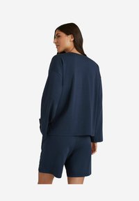Navy-blaues Loungewear-Set bestehend aus einem lockeren Langarmoberteil und passenden Shorts, hergestellt aus weichem Stoff mit glatter Textur.