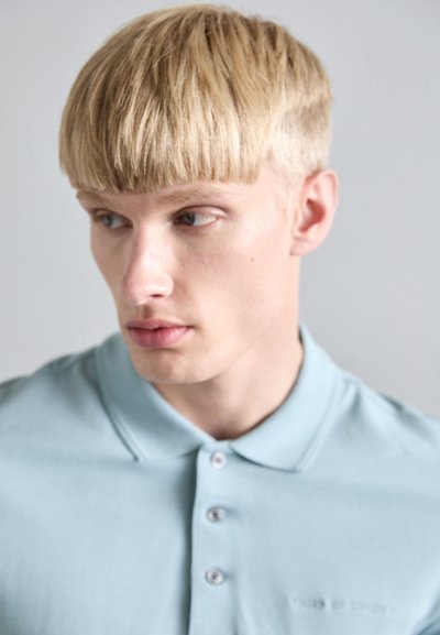 Svetlo modra polo majica z teksturirano tkanino. Ima klasičen ovratnik in tri gumbe na placketu. Subtilno blagovno znamko na prsih.