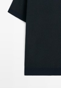 Primo piano di un tessuto a maglia strutturato blu navy scuro manica corta con polsini e orlo finemente a coste.