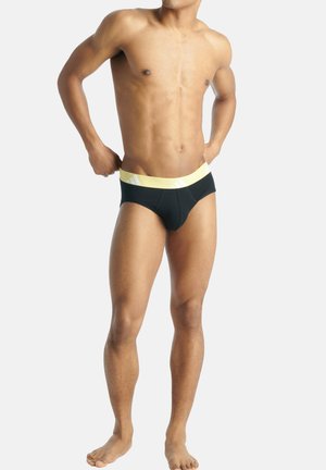 Schwarze Badehose mit gelbem Bund, der diagonale weiße Streifen aufweist, aerodynamisches Design und glatte Textur.