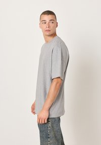 Šedé bavlněné tričko s krátkými rukávy, volným střihem, kulatým výstřihem a hladkou texturou, doplněné modrými džínami z denimu.