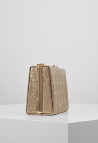 Borsa a spalla con texture dorata e forma rettangolare strutturata. Presenta una chiusura metallica e un elegante dettaglio con zip verticale.