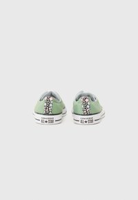 Grønne lerrets sneakers med blomstermønstrede hæl-tabs, hvide gummisåler og sorte striber. Har "Converse All Star" branding på hælen.